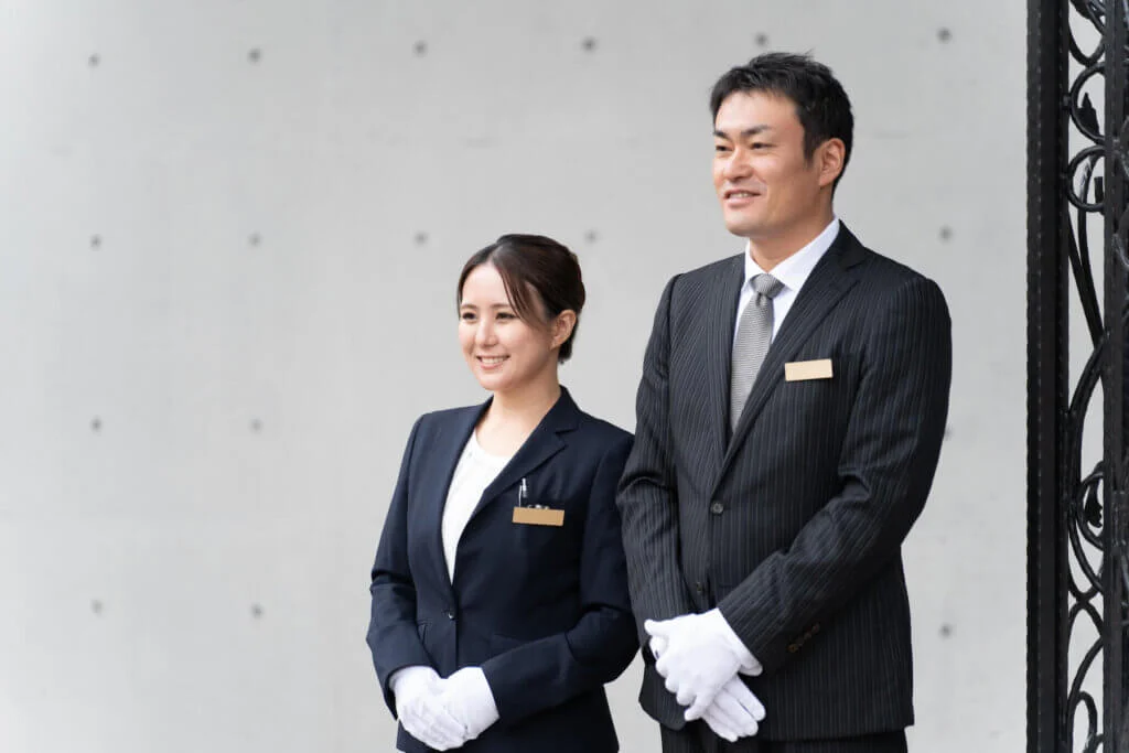 結婚式場の男性と女性2人のスタッフが並んで立ち、微笑みながら1箇所を見つめている