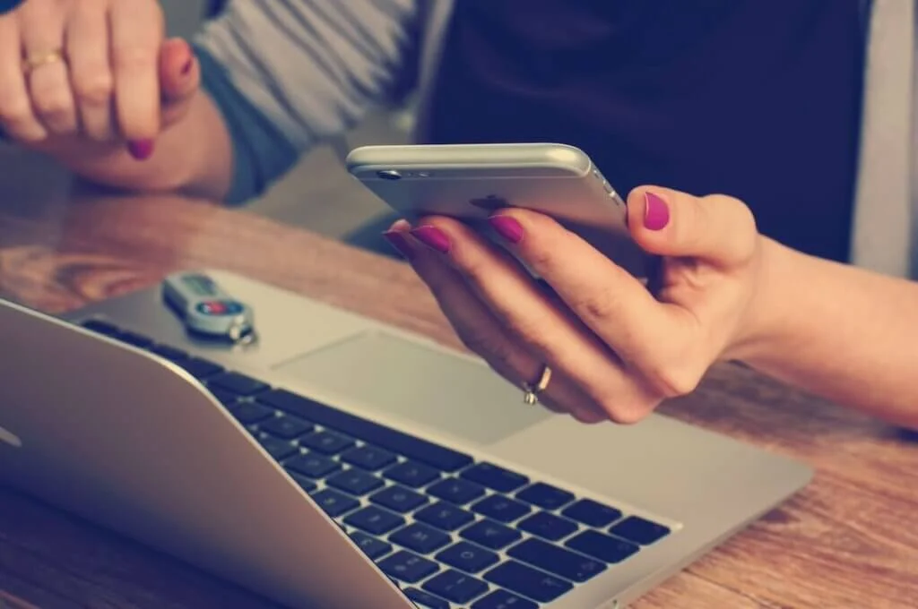 スマホを片手にMacで調べ物をする女性
