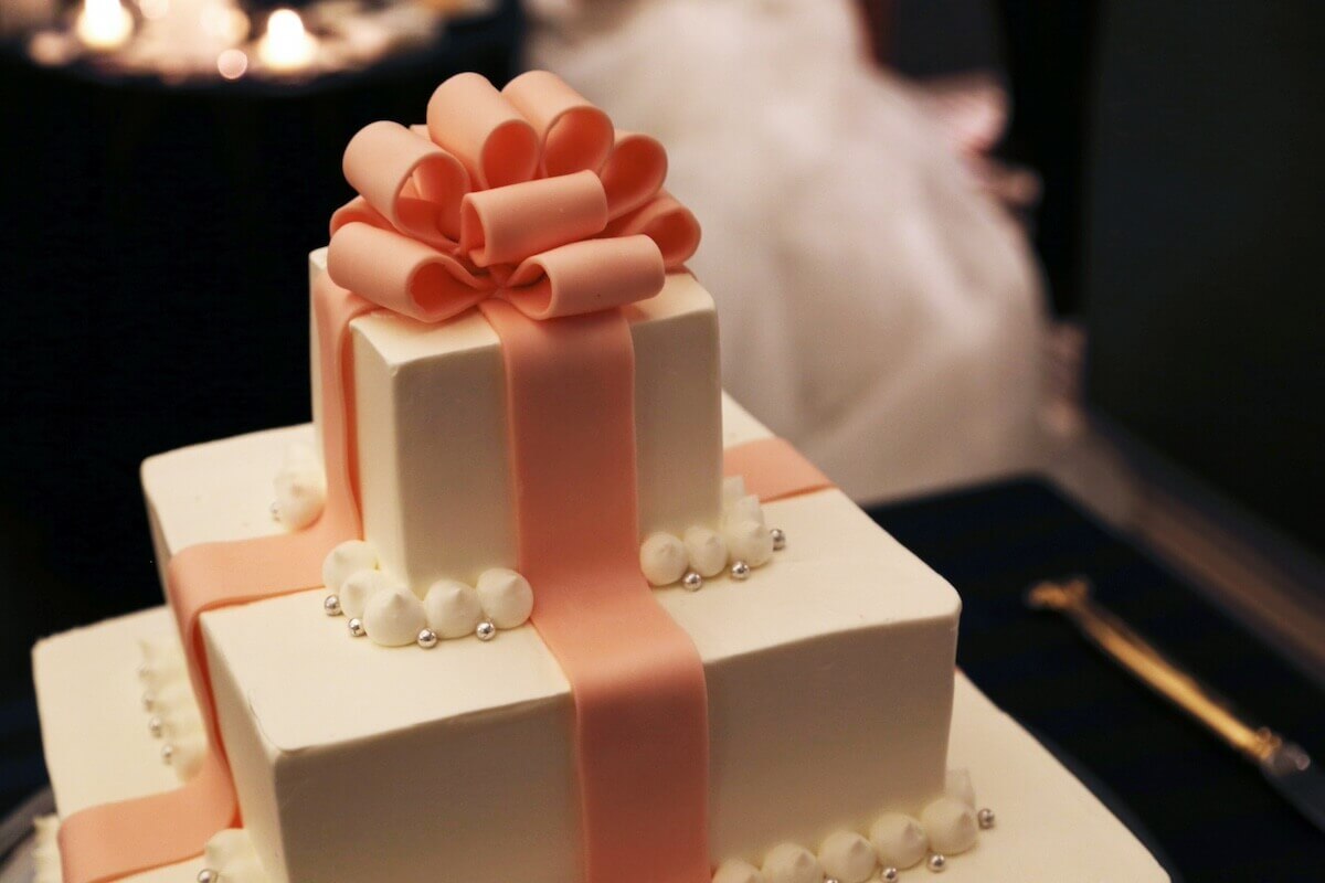 ピンクのリボンがかかったようにデコレーションされた3段のウェディングケーキ