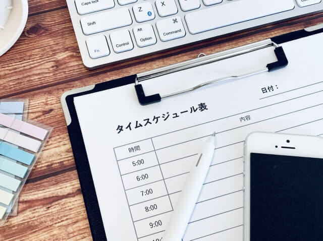 バインダーに挟まれたタイムスケジュール表とスマートフォンとボールペン