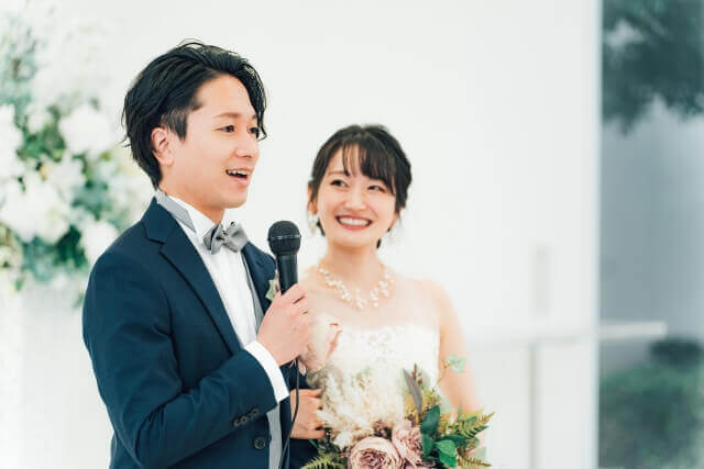 二次会参加者に挨拶する新郎とその横に満面の笑顔での佇む新婦