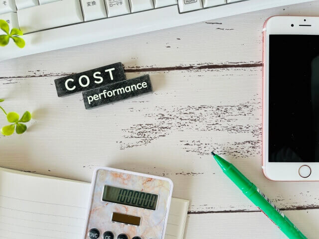 アルファベットでCost performanceと書かれたプレートとスマホと電卓が置かれた画像