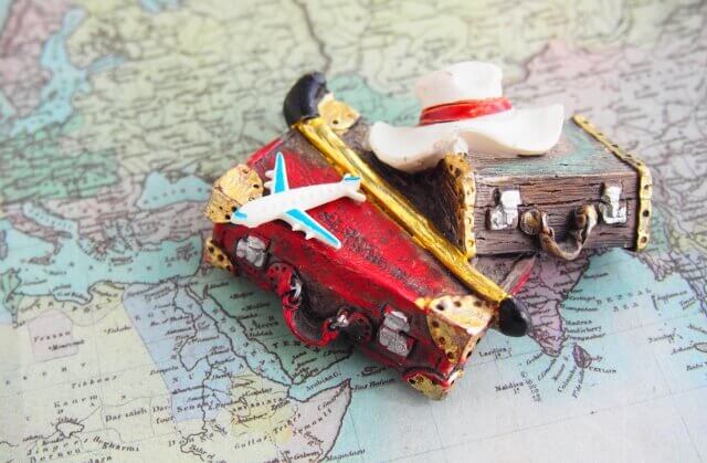 ミニチュアの木製のバックの上に、小さな飛行機と小さなハットが地図の上に置かれている
