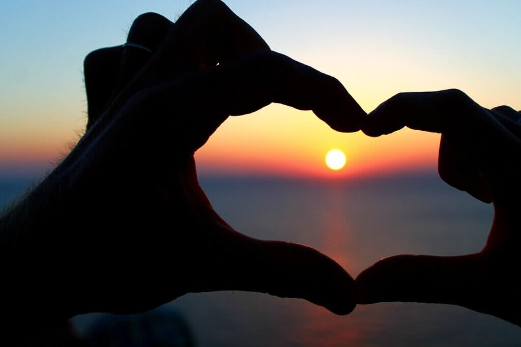 ハート型にカタチ取っ指の中に夕日が表示されている