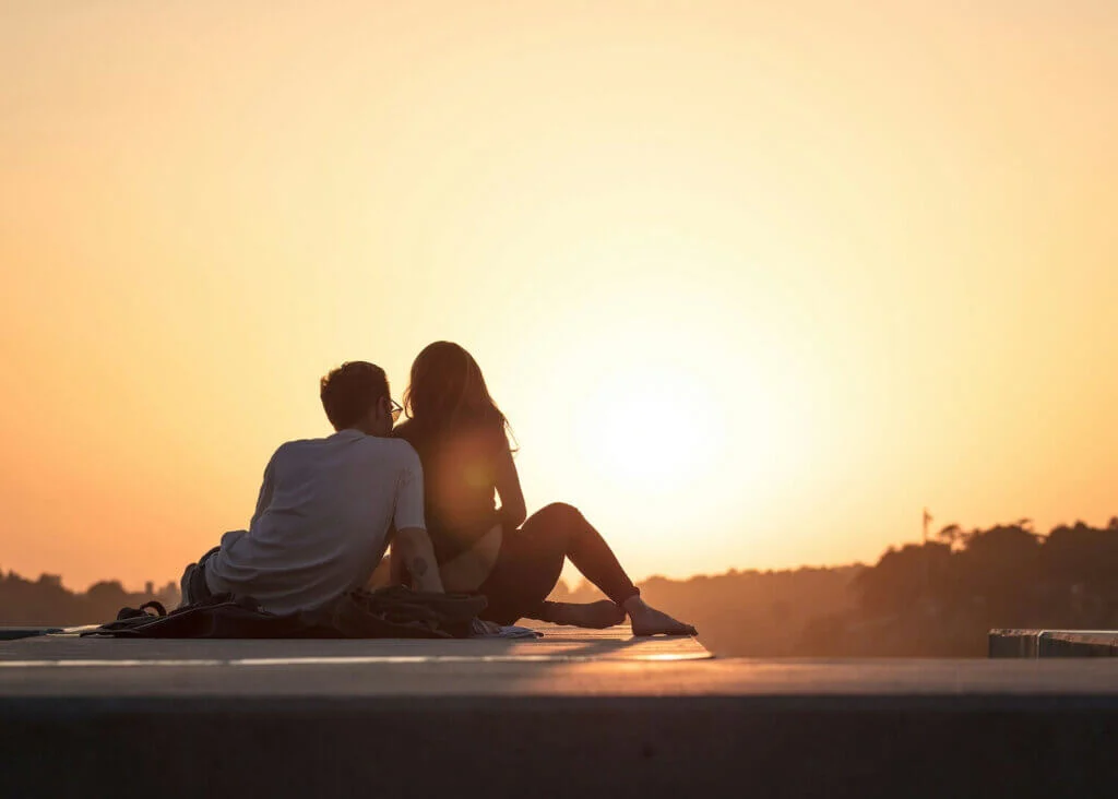 夕日の海辺で、肩を寄せ合って座っている新婚カップル