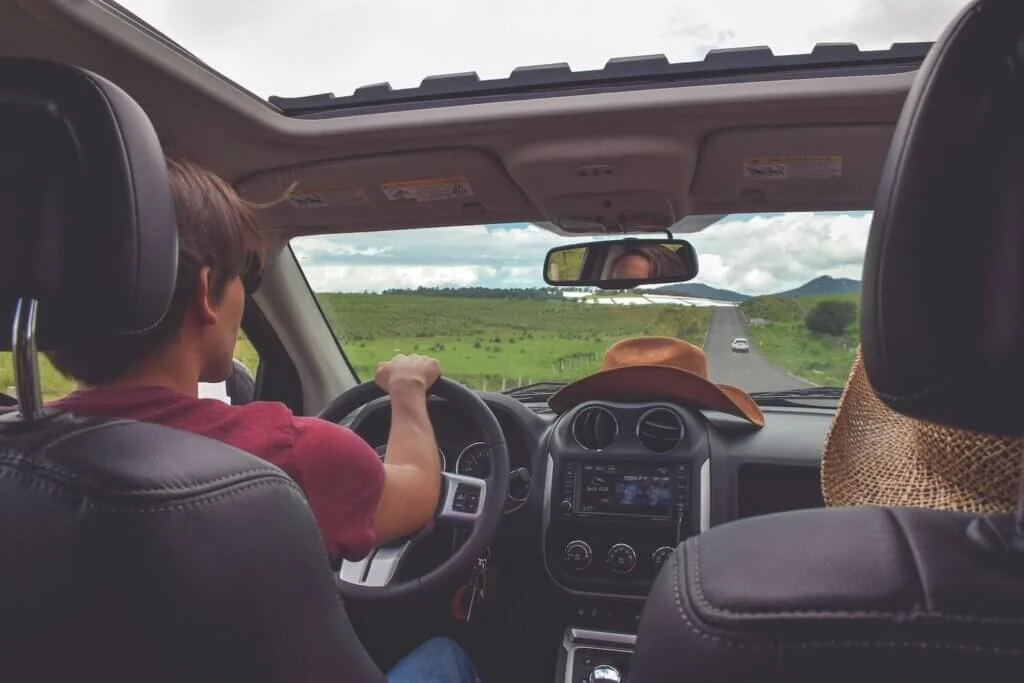海外の草原の間を抜ける道を運転するカップル