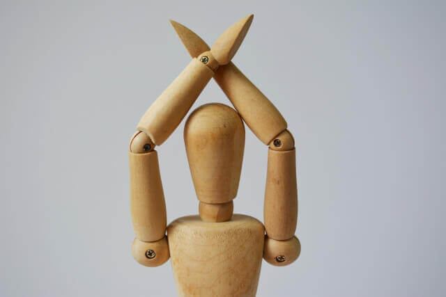 頭上で腕を交差してバッテンを表現している木製のマリオネット