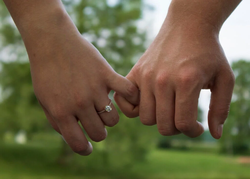 婚約指輪がはめられた手と手を小指で繋いでいるカップルの手元