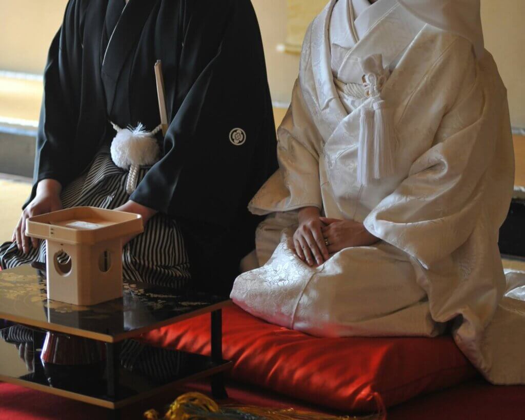 仏前式で出席者のほうに向き正座している羽織袴と白無垢姿の新郎新婦