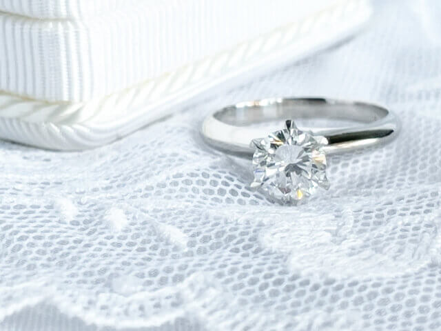 白いレースの上に置かれた大きなダイヤモンドが配置されている婚約指輪