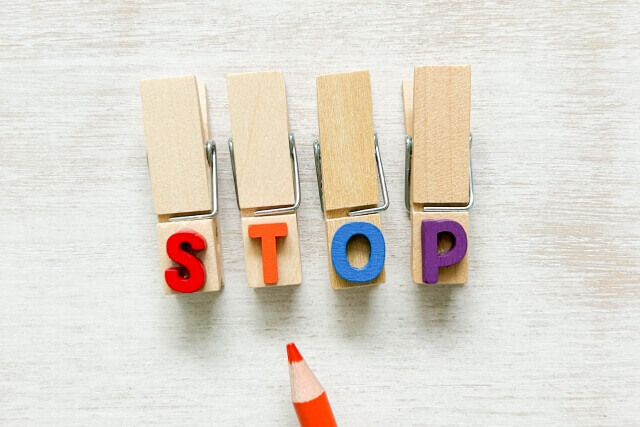 4つのウッドペグに配置されたSTOPの文字とオレンジ色の鉛筆