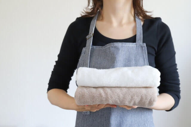 洗い上がって綺麗に畳まれたタオルを手に持つエプロン姿の女性
