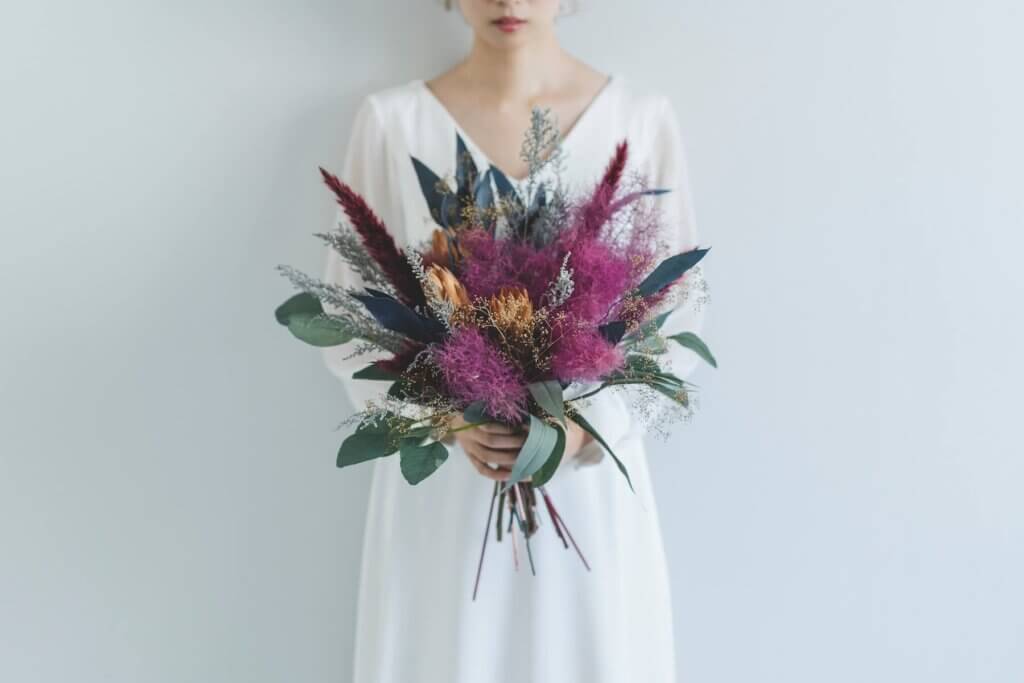 紫とオレンジ、深い緑色など、個性的な色でコーディネートされたスタイリッシュなブーケ