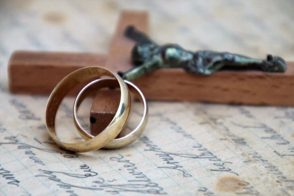 キリストの十字架に重ねられた金色の結婚指輪セット