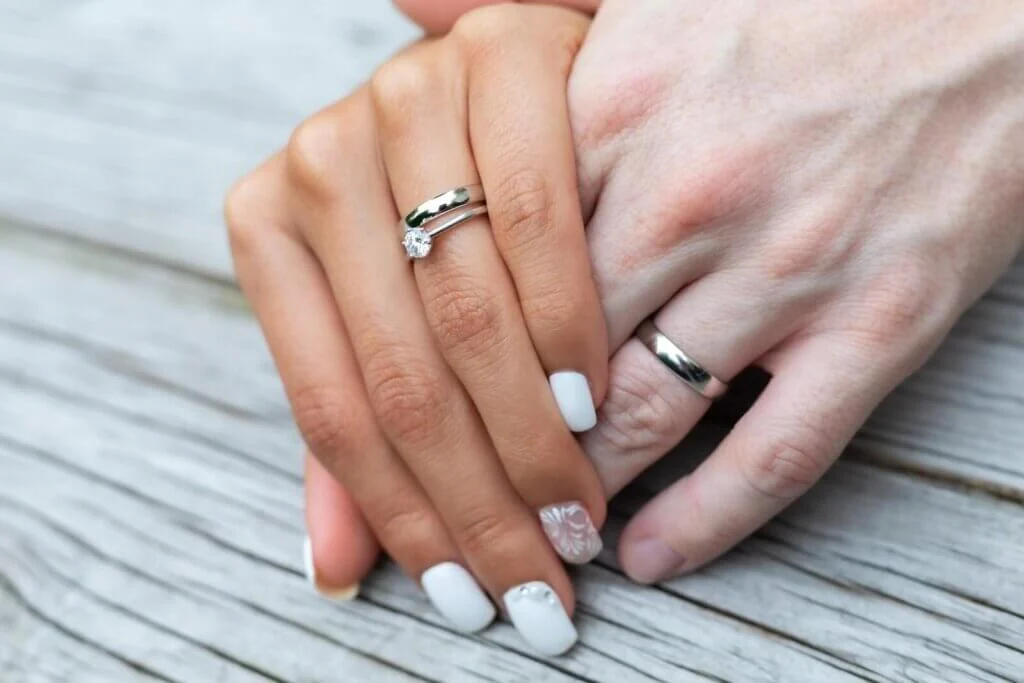 結婚指輪をはめた男性の手を握りしめている結婚指輪と婚約指輪の両方をはめた女性の手