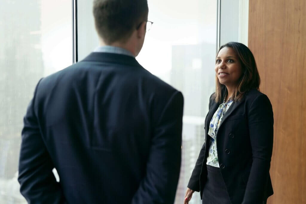 オフィスの窓際で笑顔で同僚の男性に話しかけている女性
