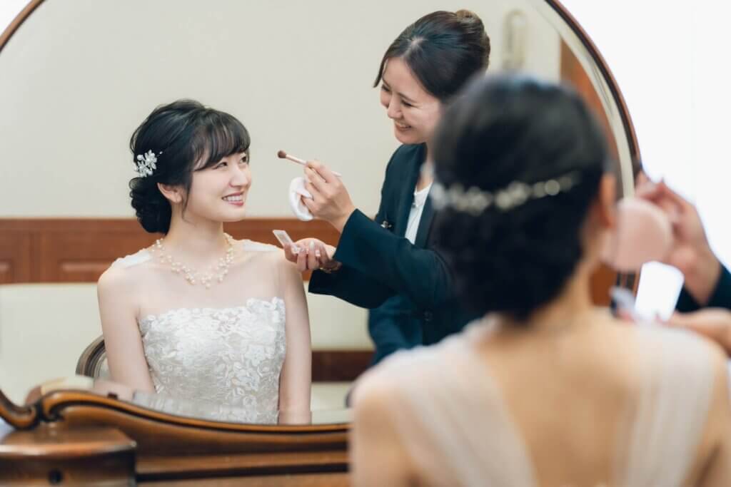 結婚式場の担当者からヘアメイクを受けているウェディングドレス姿の新婦