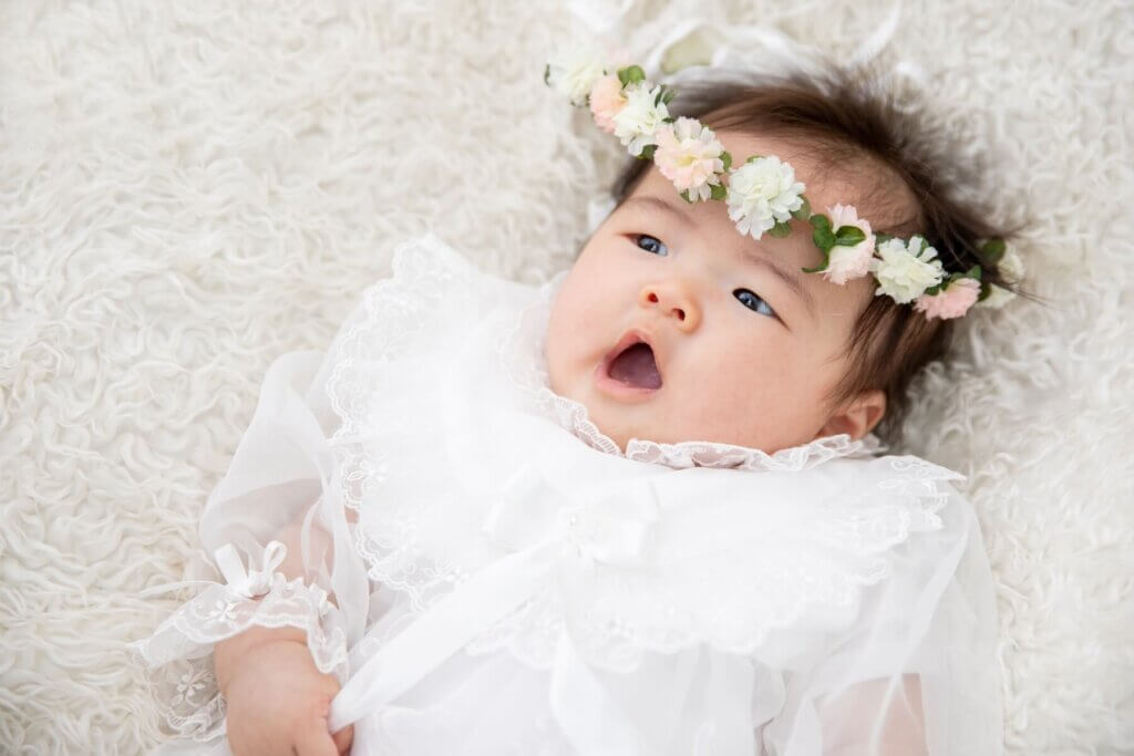 白いレースのかわいいドレスとお花の髪飾りをした赤ちゃん