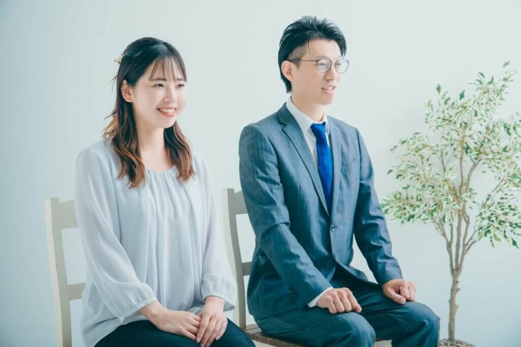 2人並んで椅子に座り、笑顔でこちらを向いているカップル