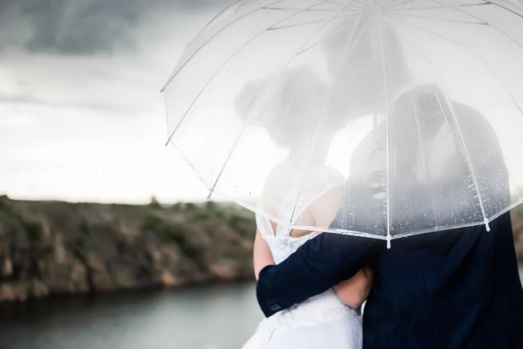 雨の中、傘をさしながら、キスをする新郎新婦