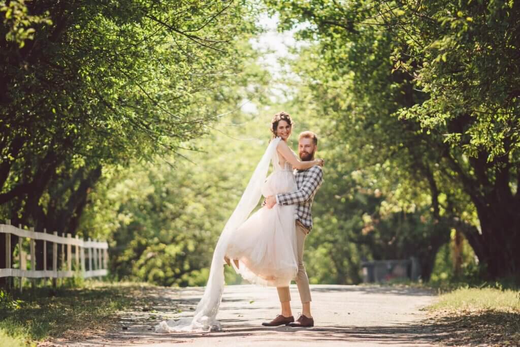 森の中の小道で、ウェディングドレス姿の新譜を抱き上げる、カジュアルなスタイルの新郎