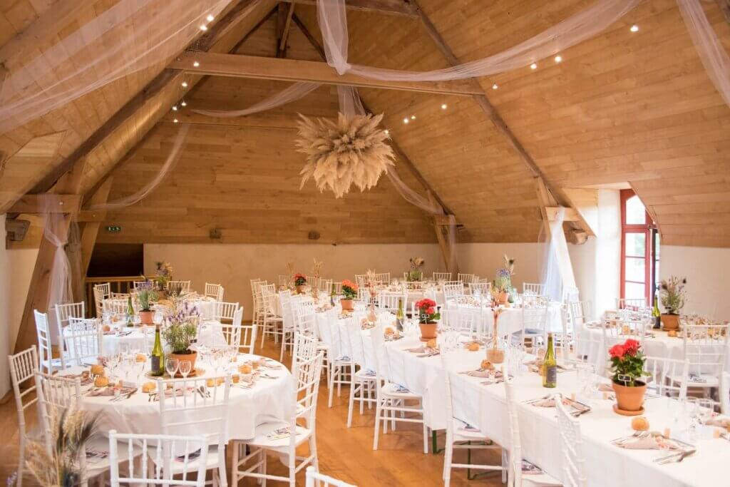 木製の斜めの天井と白い壁といったナチュラル素材の屋内で、白を基調にしたテーブルウェアで飾られた披露宴会場
