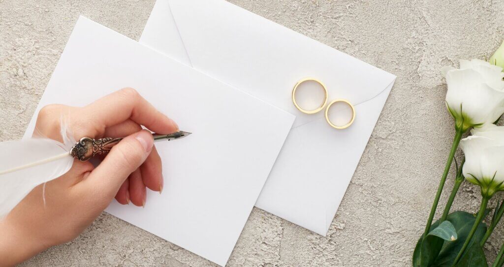 白い封筒に宛名を書こうとする左手と封筒の上に、乗せられたいついの結婚指輪。