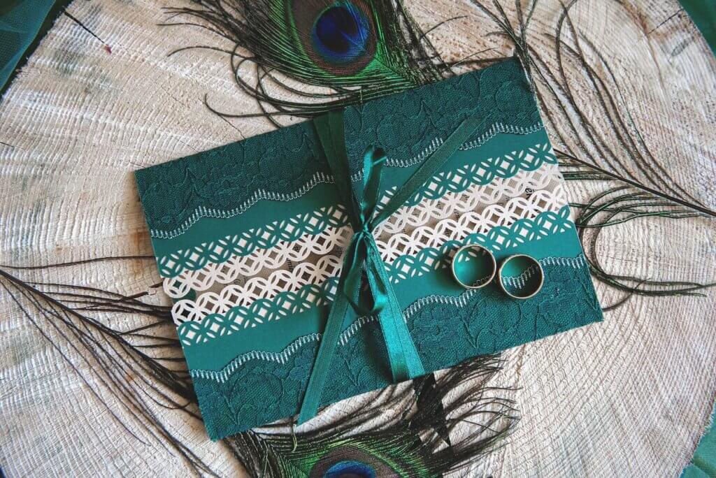 緑色のデザインがあしらわれた、おしゃれな封筒に入れられた結婚式の招待状。その上にいついの結婚指輪が載せられている。