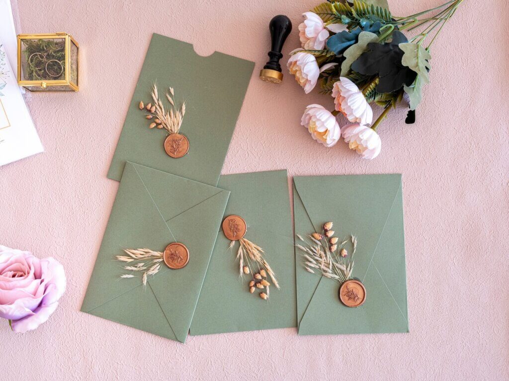 おしゃれなデザインがあしらわれた、緑色の封筒と花束と結婚指輪