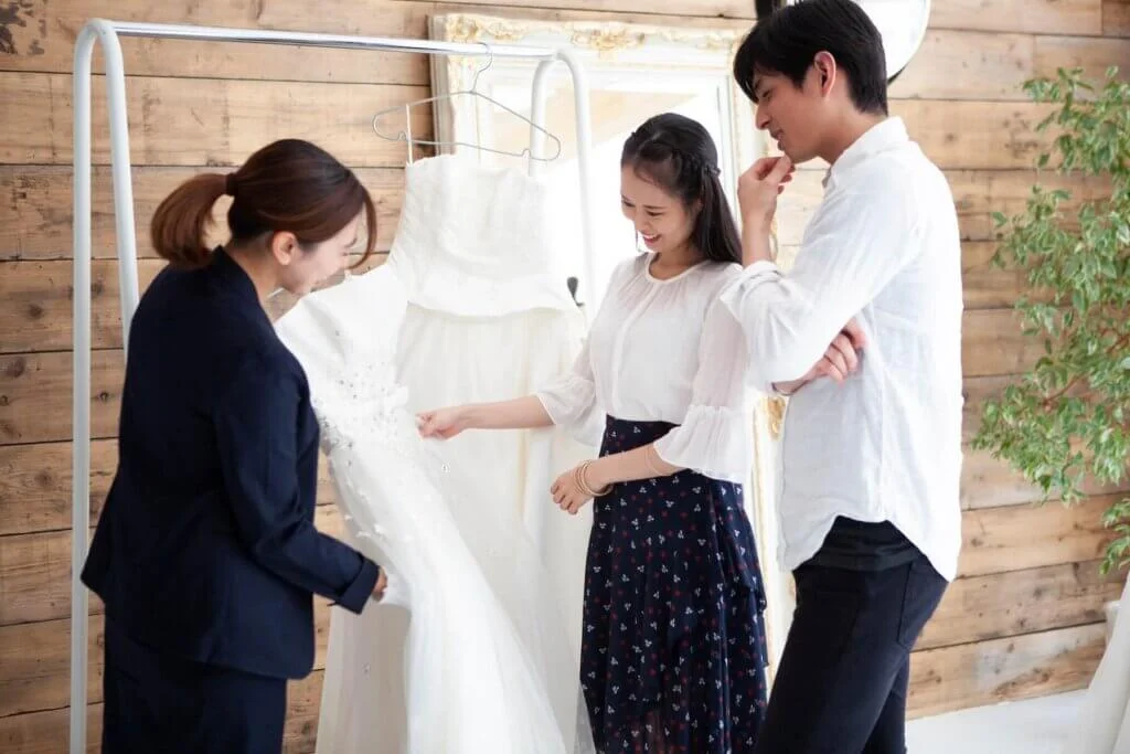 ウェディングドレスを新郎と新婦に向かい見せながら説明をしているウエディングプランナー