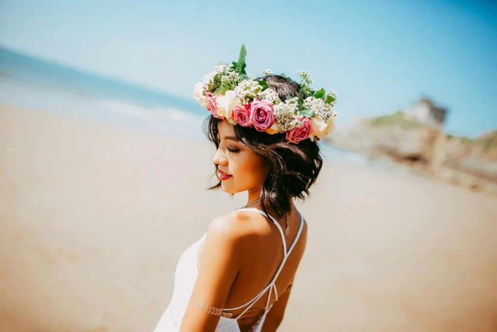 鮮やかな花飾りのティアラをつけ、純白のウェディングドレス姿でビーチに佇む新婦