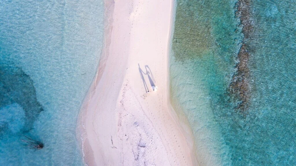 モルディブの砂浜の島でジュンお悪のドレスとスーツに身を包んだカップルを空撮している写真