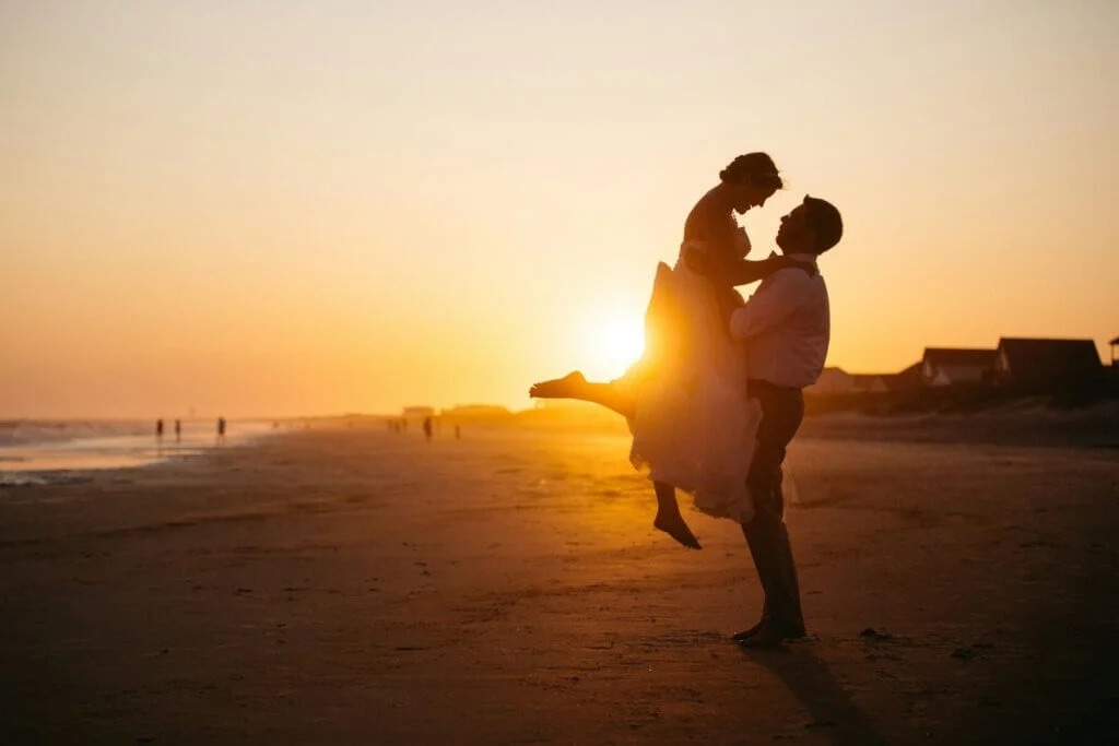 オレンジの包まれる夕日を背景に新婦の腰を持ち、抱き上げる新郎