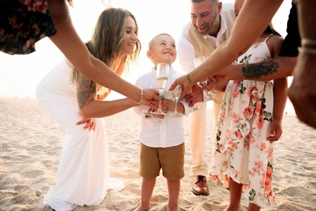 小さな男の子を囲んで、ビーチで乾杯する新郎新婦と出席者達