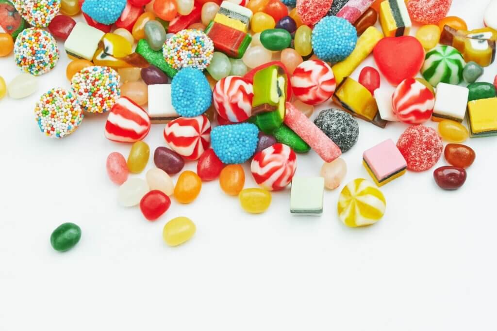 赤や黄色、白、水色など、カラフルなたくさんの種類のキャンディーやグミが白い机の上に広げられている