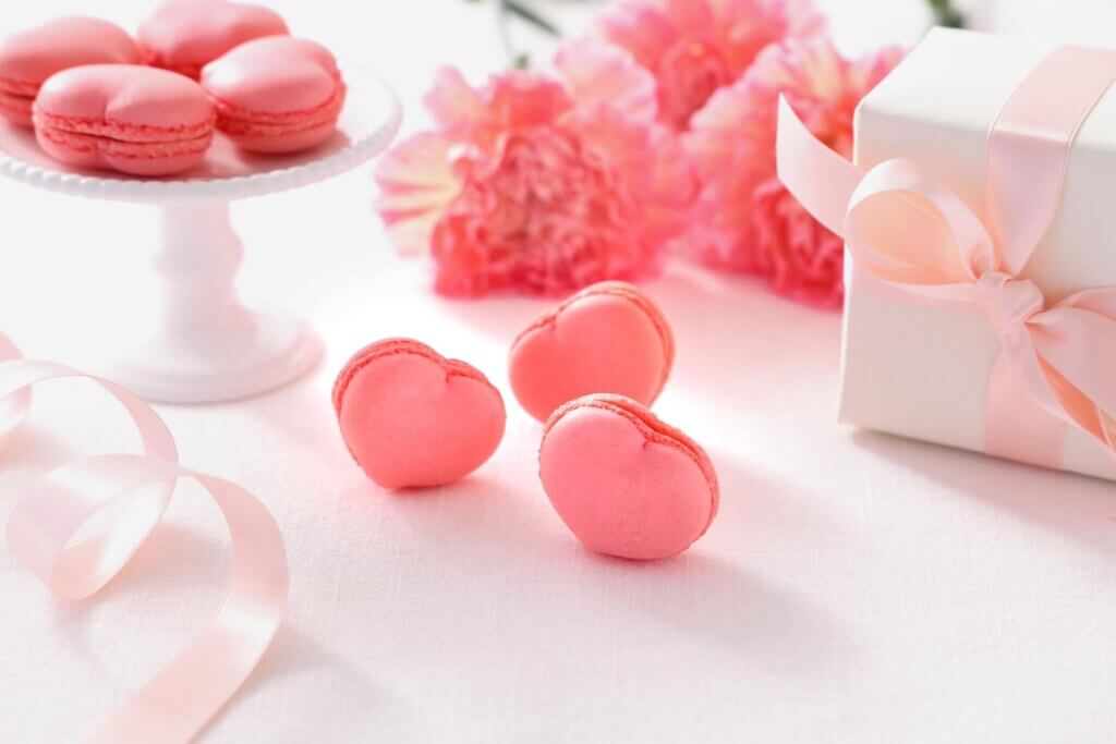 ハートの形をしたピンク色のマカロンが取り皿の上に並べられており、その手前に3つの同じハート型のマカロンが並べられている
