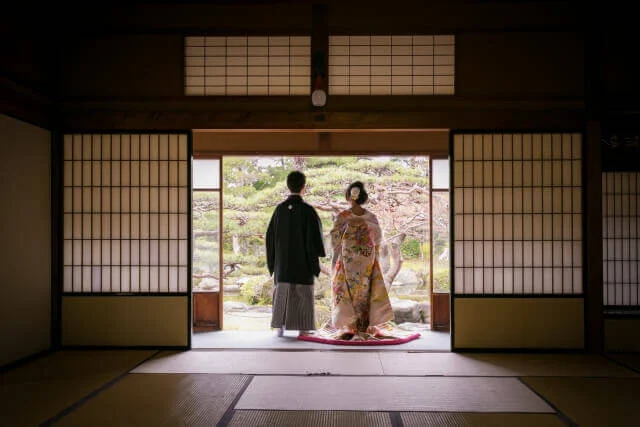 和の庭園を縁側に立って眺めている羽織・袴姿の新郎と色打掛の新婦