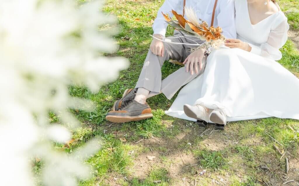 カジュアルなタキシードとシンプルなウェディングドレスに身を包み、芝生の上に座っている新郎新婦