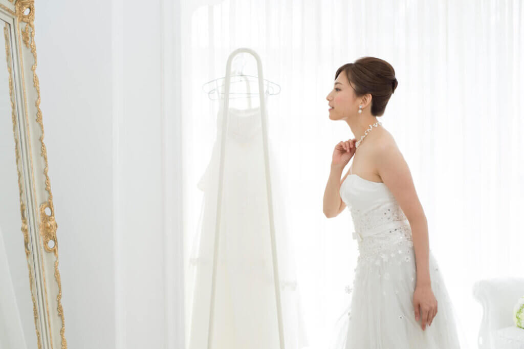 ウェディングドレス姿の新婦が胸元のネックレスを手に持ち、鏡を見て自分の姿をチェックしている