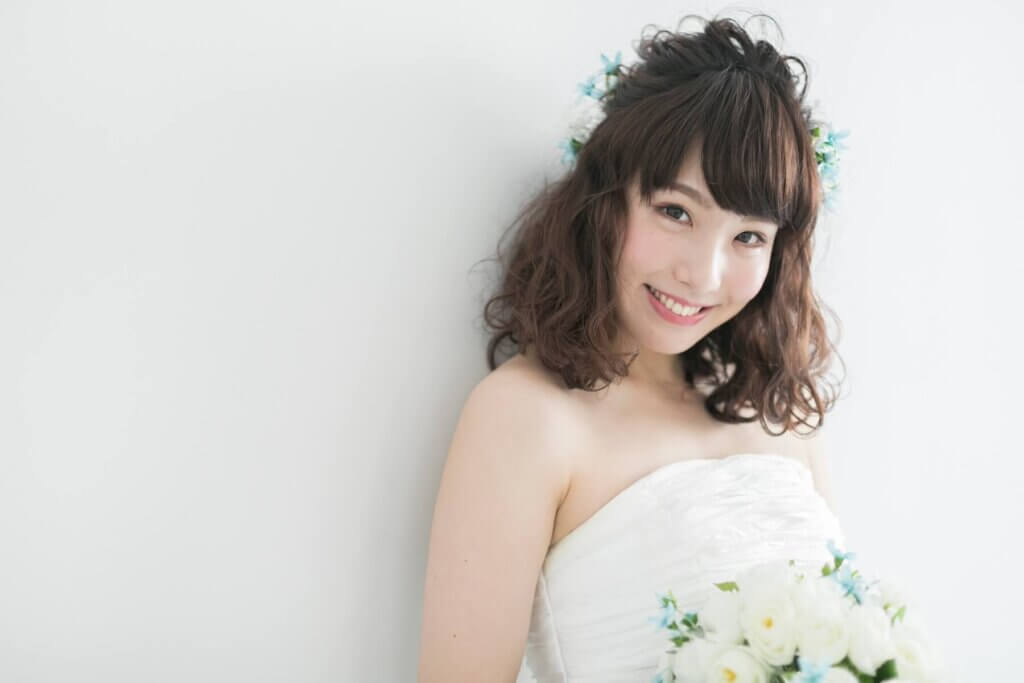 白いブーケを持ち、ウェディングドレスに身を包んでいる新婦がこちらを見て微笑んでいる。