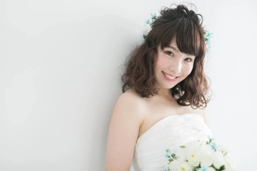 白いブーケを持ち、ウェディングドレスに身を包んでいる新婦がこちらを見て微笑んでいる。