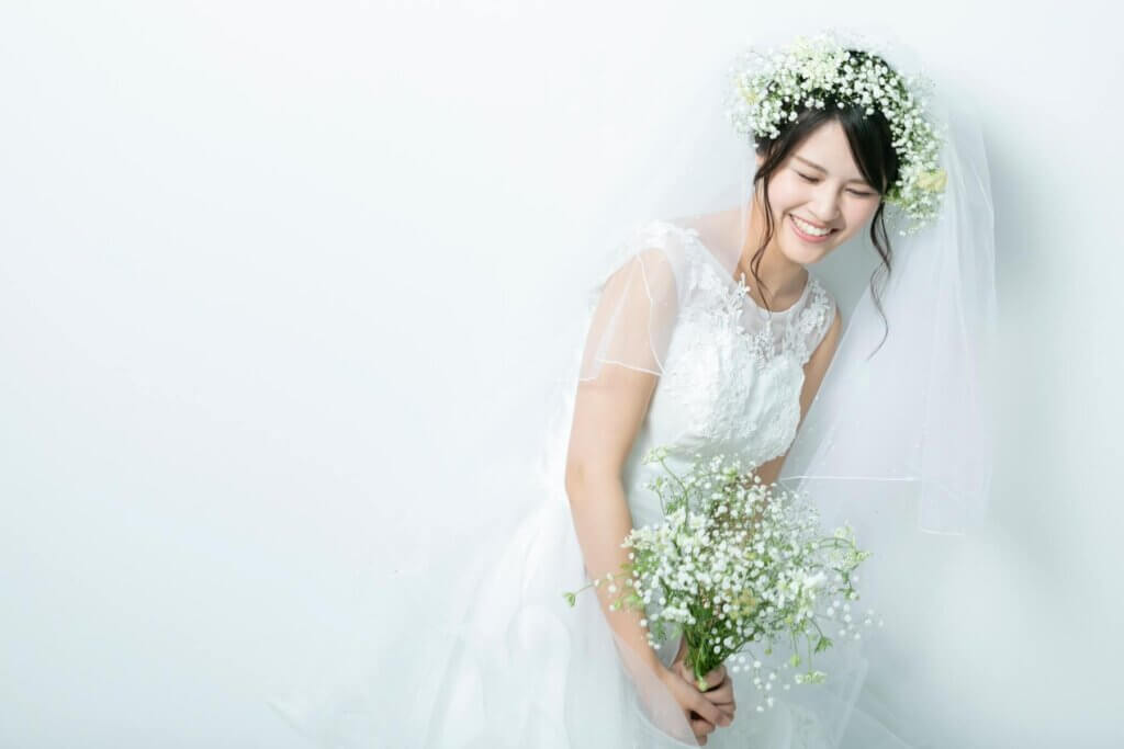 前かがみで、微笑んだポーズをとり、ウェディングドレスに身を包む新婦
