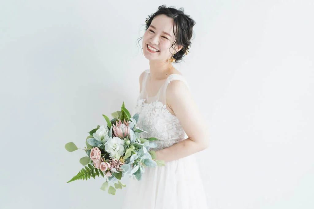 白いドレスに身を包み、カラフルなブーケを持って、こちらを見て笑っている新婦