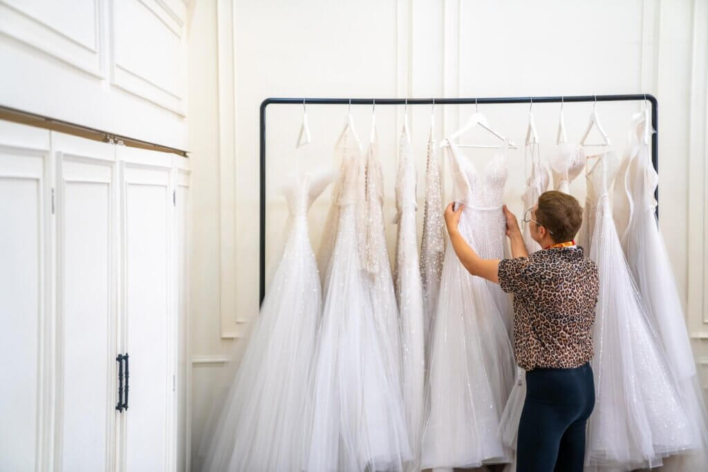 ハンガーに吊るされて並んでいるウェディングドレスを選んでいるドレスコーディネーター
