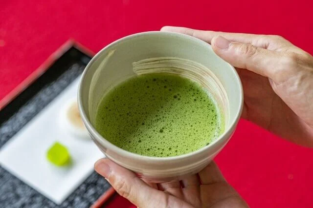 たてられた抹茶を飲もうとして、両手で器を持ち上げているところ
