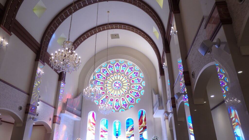 水色と紫で飾られたステンドグラスが中央に配置されている真っ白な内装のチャペル。