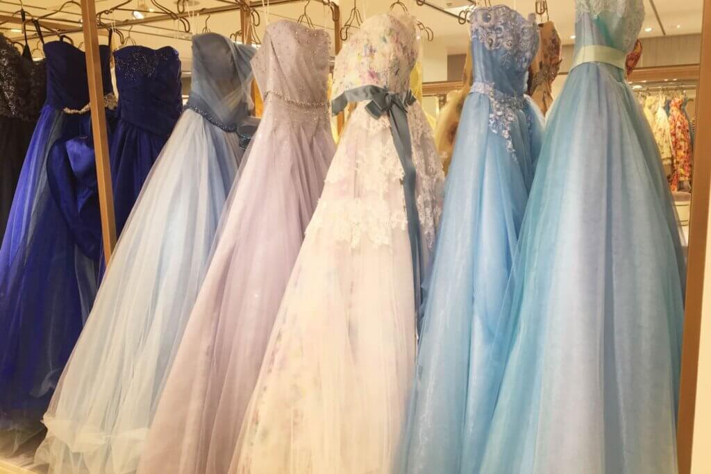 ドレスショップで並べられているカラードレスの数々。ブルー、グリーン、ピンク、パープル、ネイビー、ブルー等のドレスが吊り下げられている。