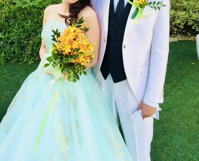 明るく、淡いグリーンのドレスに身を包み、白いタキシードの新郎に寄り添っている新婦。