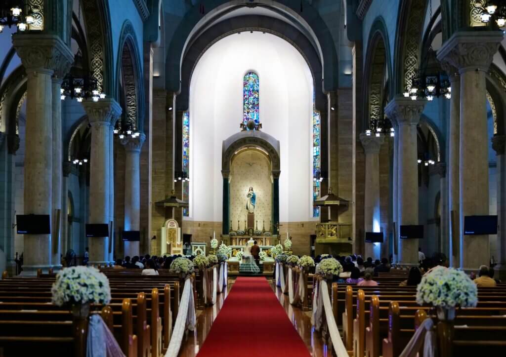 長く赤いバージンロードの奥で祈りを捧げている新郎新婦と列席者