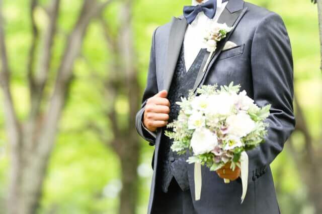 森の中で白いブーケを持ち佇むグレーのタキシード姿の新郎